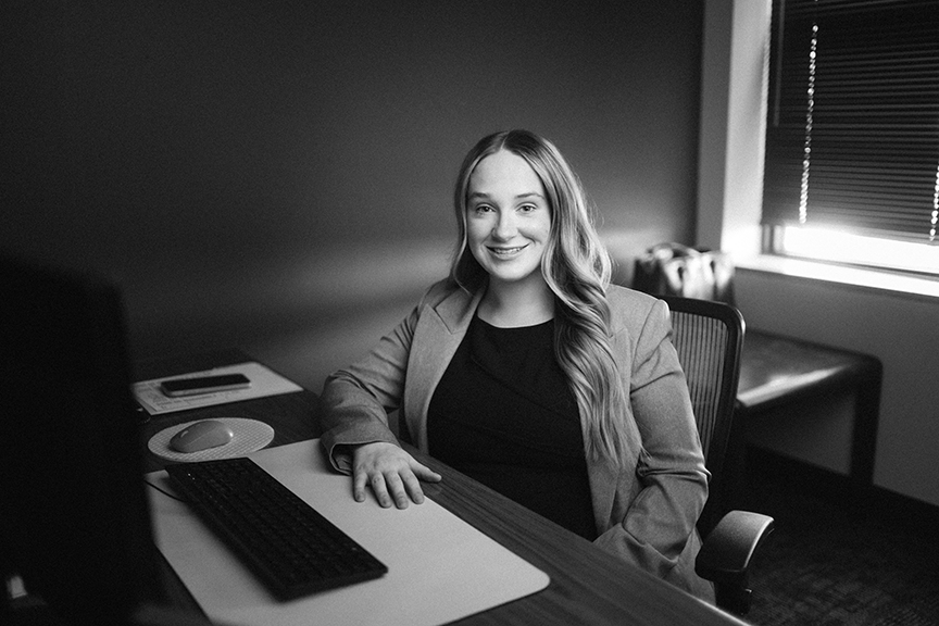 Black and white image of Rachel Sams sitting at her desk and smiling